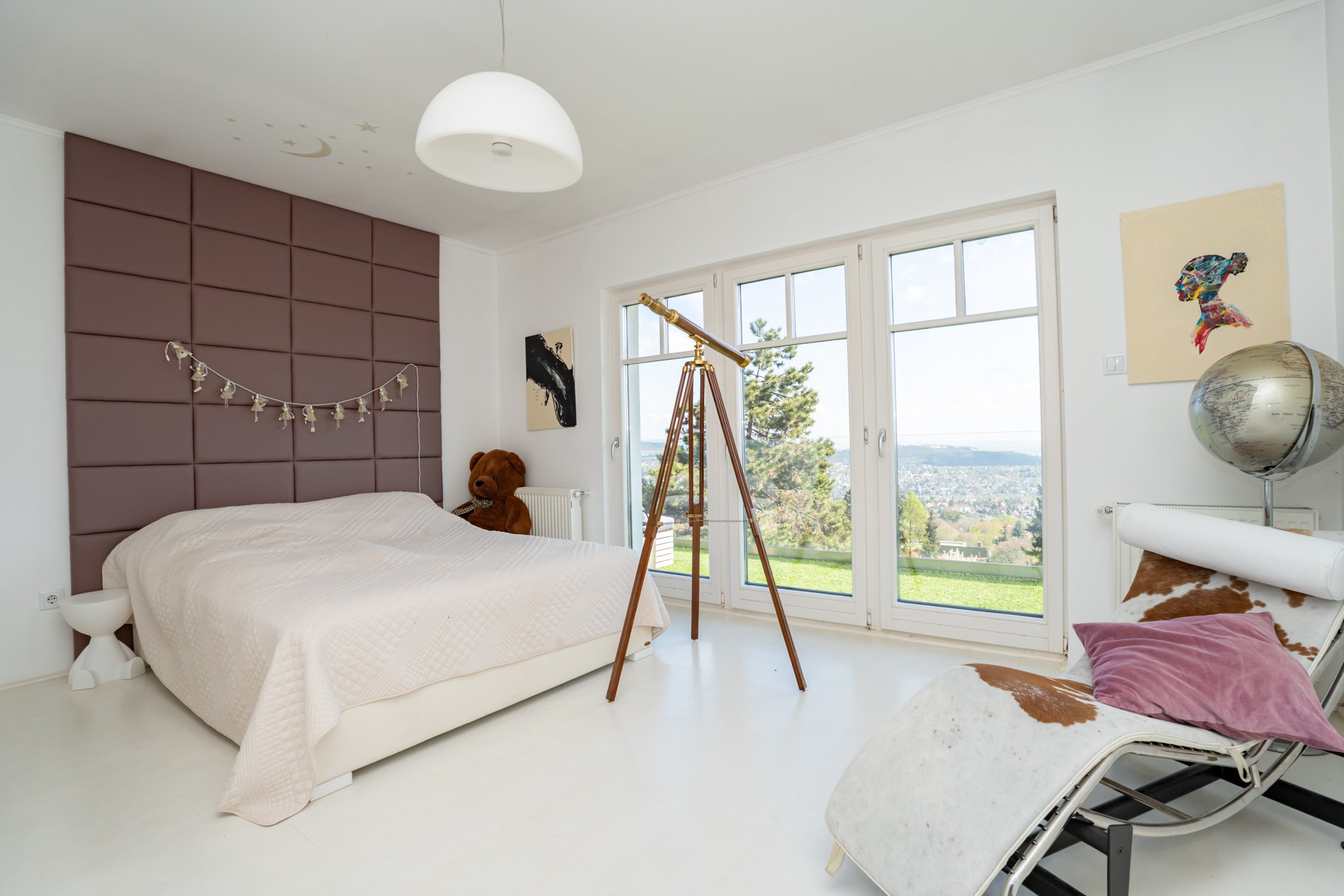 Ez egy világos, modern hálószoba nagyméretű ablakokkal, amelyek lenyűgöző panorámás kilátást biztosítanak. A szoba tiszta, minimalista fehér padlóval és falakkal, valamint egyedi berendezési tárgyakkal rendelkezik.